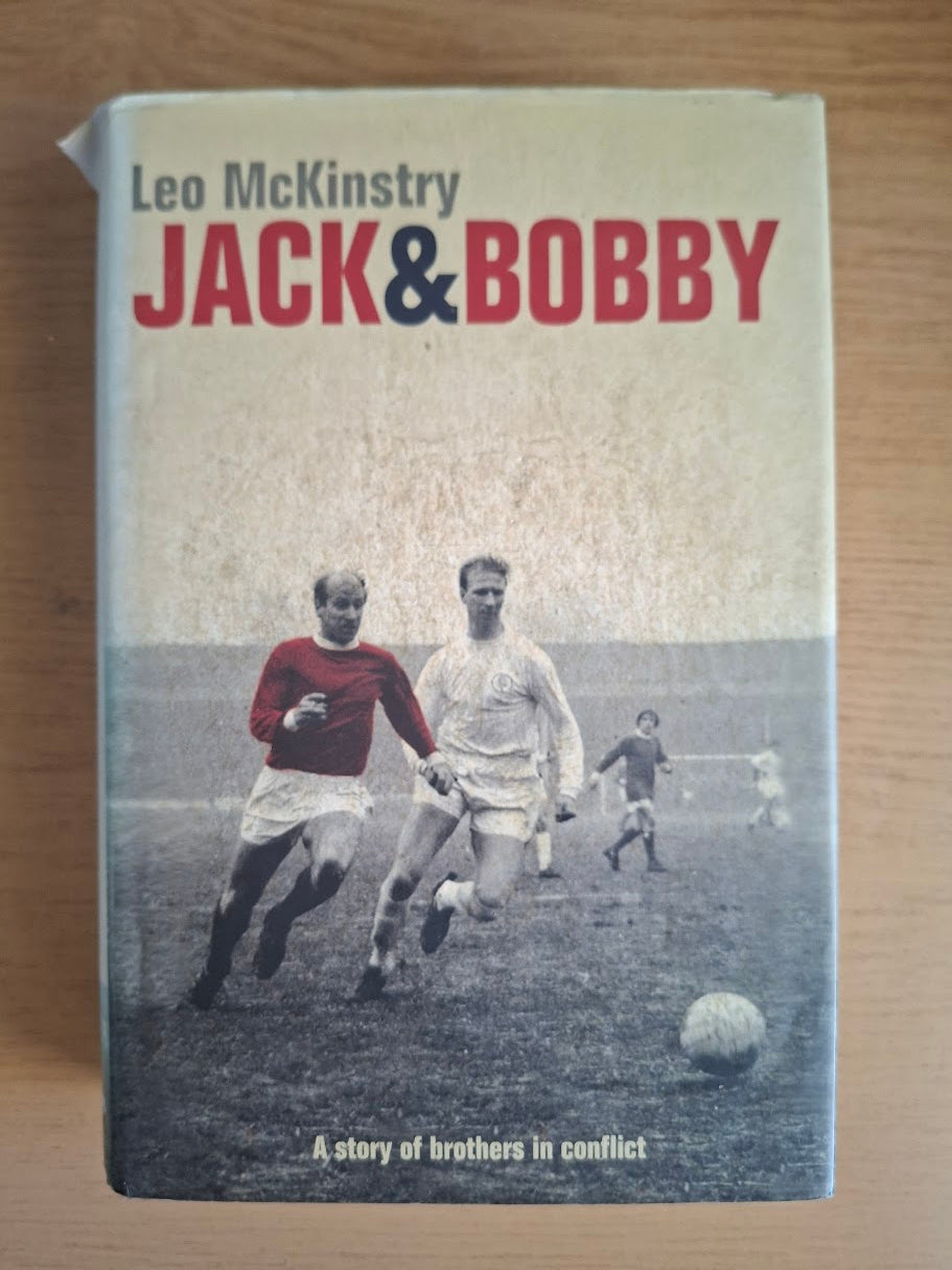 The book cover of 'Jack & Bobby' by Leo McKinstry, featuring a vintage photograph of football players on a field, placed on a wooden surface.